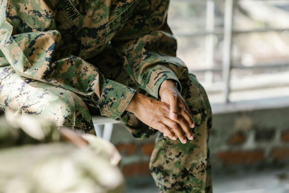 Veteran in military uniform sitting with hands clasped.