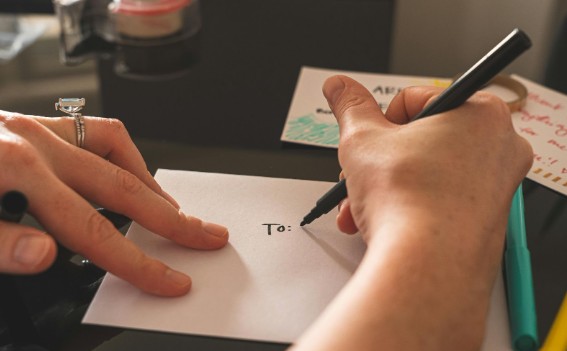 Person writing a thank-you card to a veteran, addressing an envelope by hand on a desk with cards and pens.
